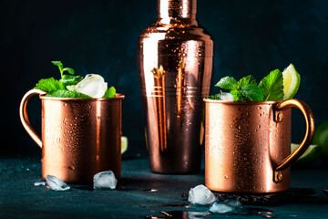 Moscow mule alcoholic cocktail in copper mug with lime, ginger beer, vodka and mint. Blue table,...