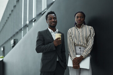 Graphic waist up portrait of two African-American business people looking at camera while standing in office hall, black and white pattern, copy space