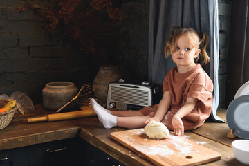 Fototapeta na wymiar A little girl sits at the kitchen table and sculpts from dough. Mom and Daughter Cook Together