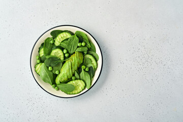 Green vegetable salad with spinach, avocado, green peas and olive oil in bowl on light gray slate, stone or concrete background. Top view with copy space. Green vegetables for diet concept.