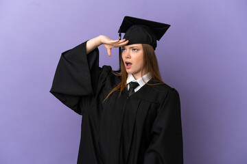 Young university graduate over isolated purple background doing surprise gesture while looking to...