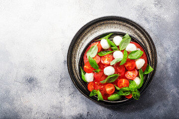 Summer caprese salad with red tomatoes and white mozzarella cheese with fresh green basil leaves. Gray table. Top view