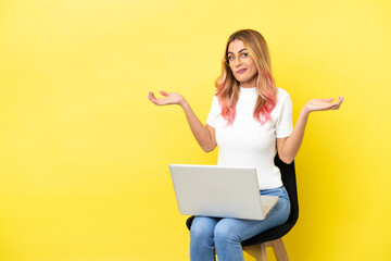 Young woman sitting on a chair with laptop over isolated yellow background having doubts while raising hands