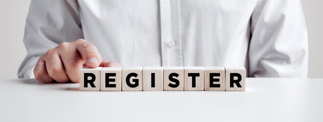 Businessman pressing his finger on the wooden cubes with the word register. registration, enrollment or subscription