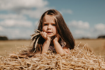 Adorable little girl in a field with haystacks.