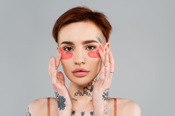 young and tattooed woman adjusting eye patches isolated on grey