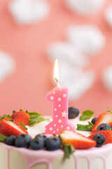 Birthday cake number 1. Beautiful pink candle in cake on pink background with white clouds. Close-up and vertical view