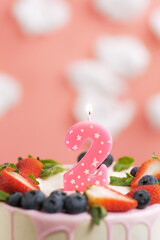 Birthday cake number 2. Beautiful pink candle in cake on pink background with white clouds. Close-up and vertical view