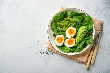 Fresh vegetable salad with avocado, asparagus, crumpled eggs with black sesame seeds and spinach on plate on light slate, stone or concrete background. Balanced lunch in bowl. Top view. Mock up.