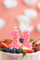 Birthday cake number 11. Beautiful pink candle in cake on pink background with white clouds. Close-up and vertical view