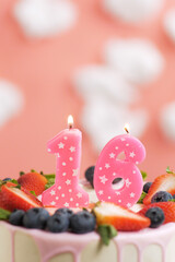 Birthday cake number 16. Beautiful pink candle in cake on pink background with white clouds. Close-up and vertical view