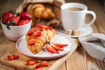 Croissant, fresh strawberries and coffee on a wooden table.