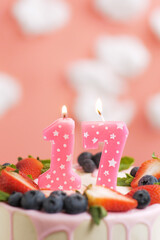 Birthday cake number 17. Beautiful pink candle in cake on pink background with white clouds. Close-up and vertical view