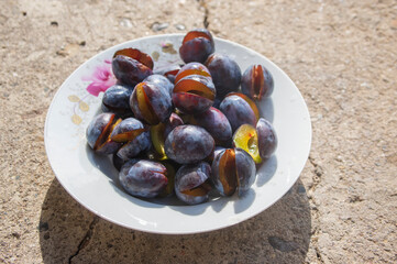 Fruits of prunus domestica tree cut in halves on vintage plate on concrete surface background in sunlight
