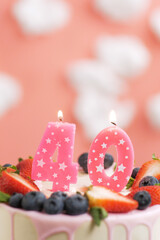 Birthday cake number 40. Beautiful pink candle in cake on pink background with white clouds. Close-up and vertical view