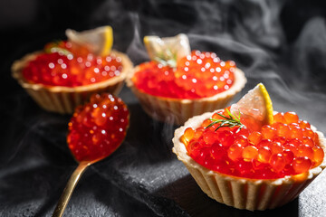 Tartlets with red caviar close-up. Red caviar among the smoke on a dark background.