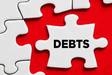 Fototapeta premium The word debts on a puzzle piece with red background. Financial debt