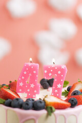 Birthday cake number 47. Beautiful pink candle in cake on pink background with white clouds. Close-up and vertical view
