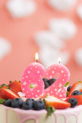Birthday cake number 62. Beautiful pink candle in cake on pink background with white clouds. Close-up and vertical view