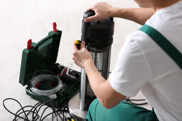 Fototapeta na wymiar Professional technician repairing electric patio heater with screwdriver indoors, closeup