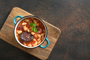 Popular spanish fabada on brown background. Fabada cooked with haricot, chorizo, morcillas or blood sausage. Top view.
