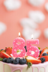 Birthday cake number 85. Beautiful pink candle in cake on pink background with white clouds. Close-up and vertical view
