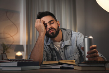 Tired young man with energy drink studying at home