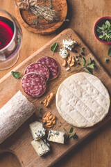 Cheese and salami aperitifs plate(wood board) with French Camembert and blue cheese, nuts, aromatic herbs and red wine. Rustic, provence style.  Winter and autumn starter or aperitifs 
