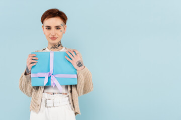 young tattooed woman holding wrapped present isolated on blue