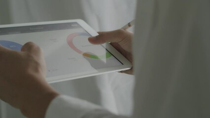 Close-up Asian businessman scrolling tablet examining financial reports and analyzing business growth at the office. - Powered by Adobe