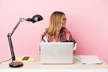 Young student woman in a workplace with a laptop over pink background in lateral position