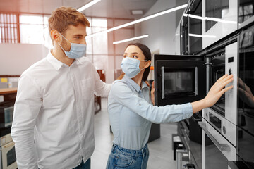 Young couple wearing medical masks in hypermarket with home appliances