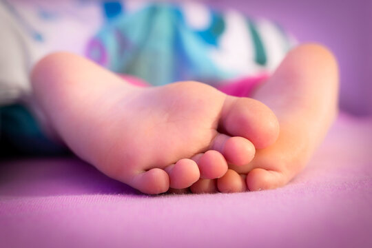The feet of a baby sleeping under the covers in bed