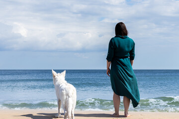 standing backwards dog swiss white shepherd with woman looking out to sea