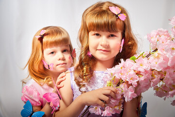 Young girls with blonde curly hair with a butterflys in the studio on a white background. Children posing during a photo shoot. The concept of spring, summer, childhood, happiness