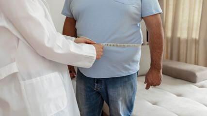 A nutritionist doctor measures the body of a male patient with a measuring tape on adipose tissue...