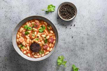 Traditional Spanish fabada served on gray background. Fabada makes of haricot, chorizo, morcillas or blood sausage, tomatoes. Top view.