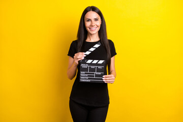 Photo of pretty positive lady hands hold clapboard beaming smile look camera isolated on yellow color background