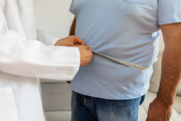Women doctor measuring overweight man in clinic. Young female doctor measuring fat layer of...