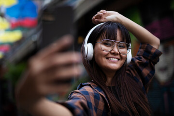 Young smiling woman outdoors. Beautiful woman listening to music while walking through the city