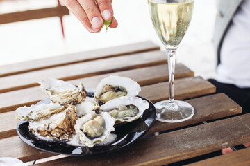 Squeezing lime juice on oysters, sparkling wine, on a wooden table on  a terrace 
