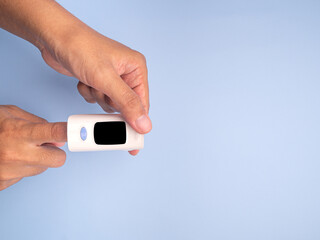 Pulse oximeter on the index finger on a light blue background. Measurement of blood oxygen and pulse. Lung disease. Close-up photo. Space for text. Healthcare concept