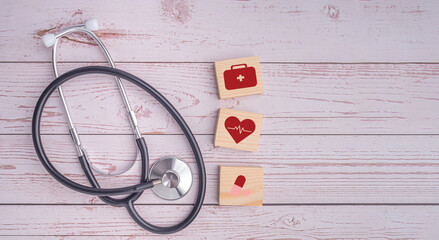 A stethoscope and wooden blocks with icons of health laid on wooden table. Close-up photo. Top view. Flat lay with Space for text. Healthcare and medicine with media icons concept