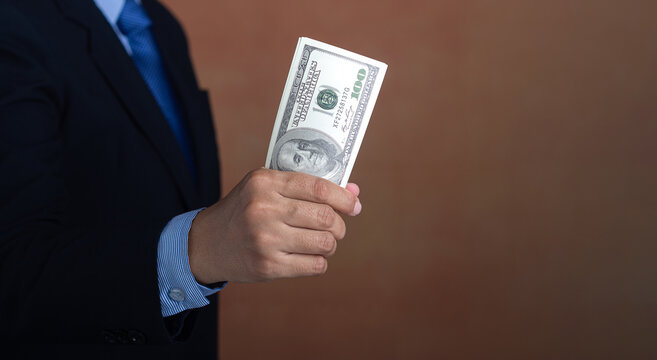 Hand of a businessman holding US dollars while standing with a brown background. Personal loans or business loans. Space for text. Close-up photo. Business and finance concept