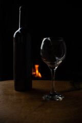Wine, wine bottle and empty glass on rustic wooden surface with fire in the background, low key image, dark background, selective focus.