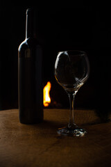 Wine, wine bottle and empty glass on rustic wooden surface with fire in the background, low key image, dark background, selective focus.