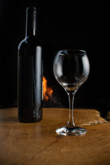 Wine, wine bottle and empty glass on rustic wooden surface with fire in the background, low key image, dark background, selective focus.