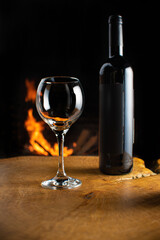 Wine, wine bottle and empty glass on rustic wooden surface with fire in the background, low key image, dark background, selective focus.