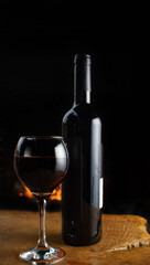 Wine, full wine glass and wine bottle on rustic wooden surface with fire in the background, low key image, dark background, selective focus.
