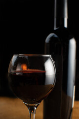 Wine, full wine glass and wine bottle on rustic wooden surface with fire in the background, low key image, dark background, selective focus.